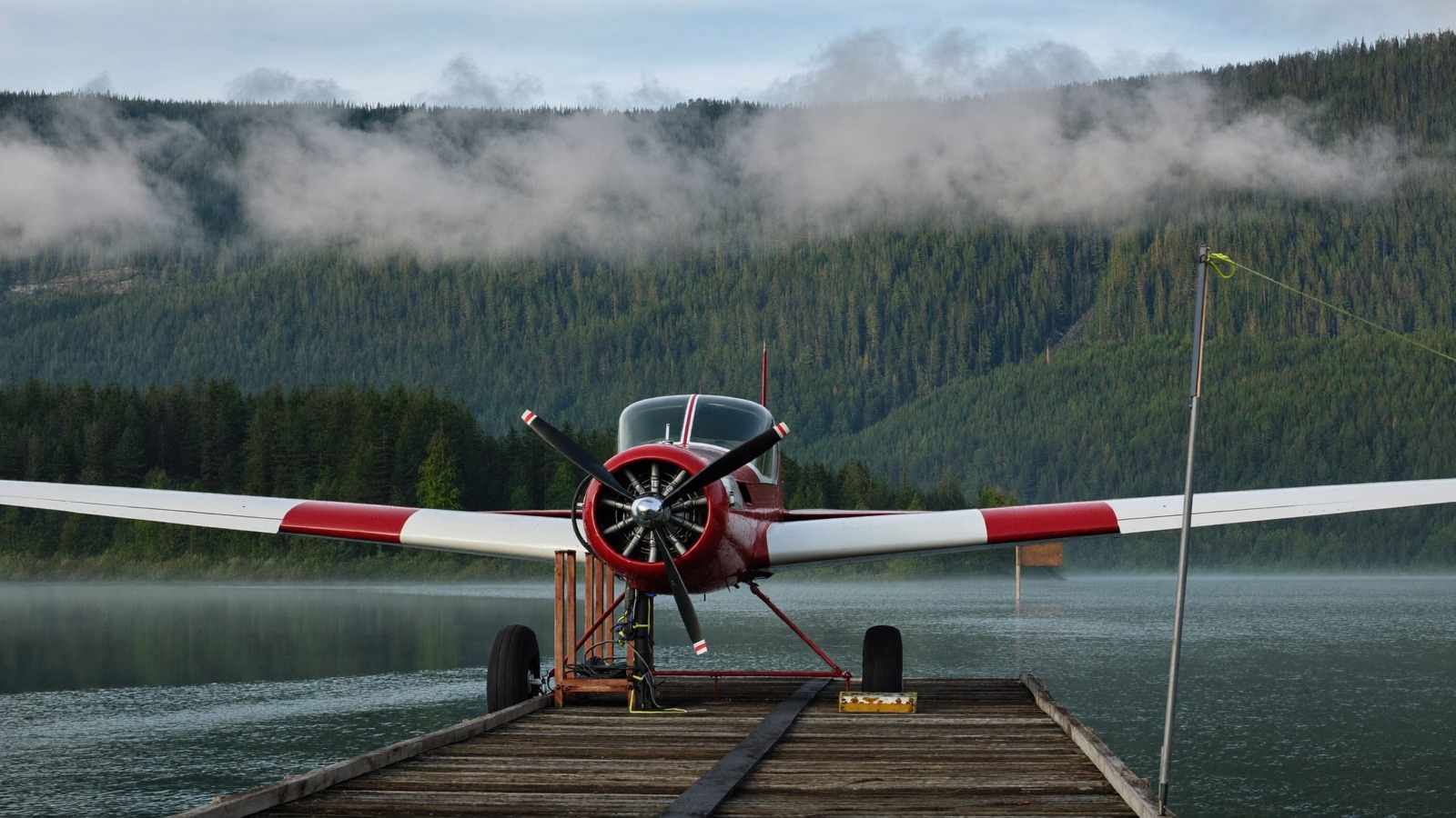 A red Kestrel Air floatplane tied up at a misty dock in a forested channel, early morning